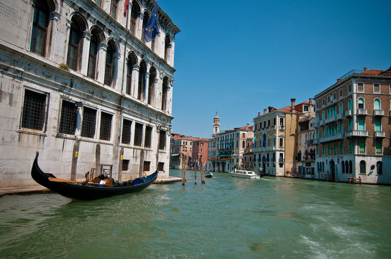 Gondola moored in grand canal amidst buildings against clear blue sky