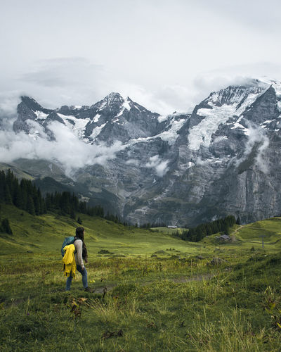 Side view of woman walking on grass against snow covered mountains and sky
