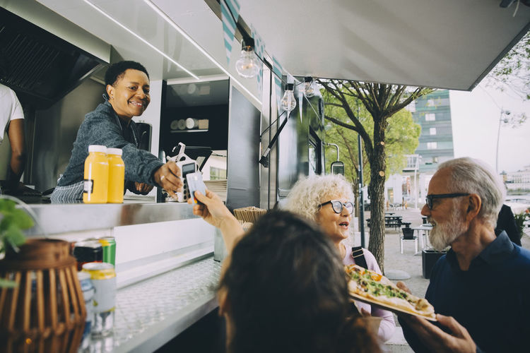Smiling owner giving credit card reader to customer for payment while standing in food truck