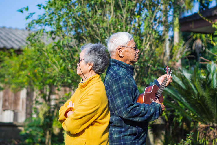 Portrait of romantic elderly man playing ukulele with his wife at home garden.