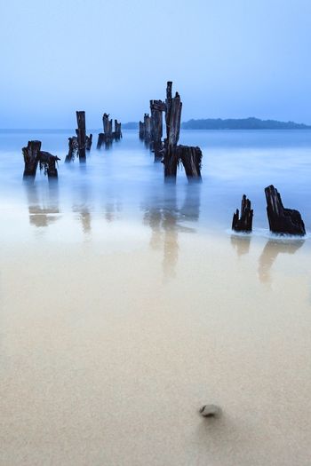 Wooden posts at beach against sky