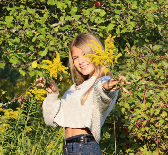 Portrait of a smiling young woman standing by plants