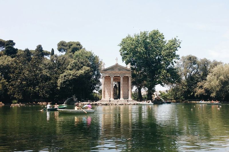 People boating in lake near temple of aesculapius at villa borghese