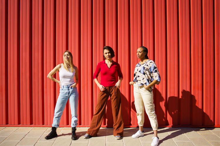Full length of happy friends standing against yellow wall