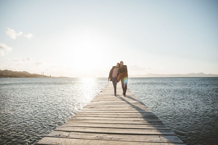 Mature couple walking on jetty over sea