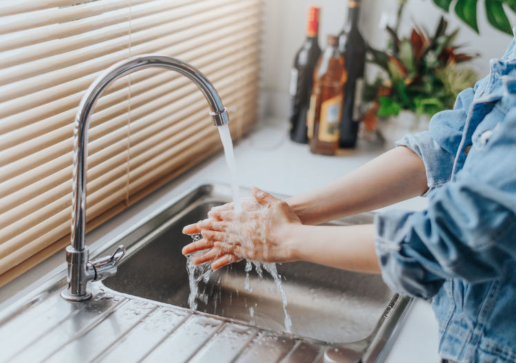 Midsection of woman washing hands in kitchen sink