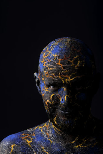Close-up portrait of mid adult man with body paint standing against black background