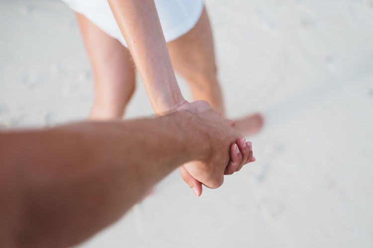 Cropped image of couple holding hands while walking at beach