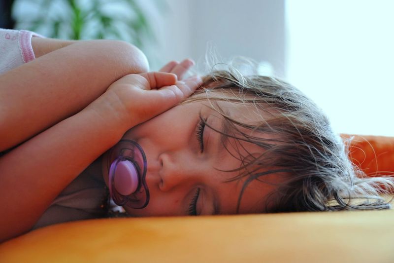 Close-up of girl with pacifier in mouth sleeping at home