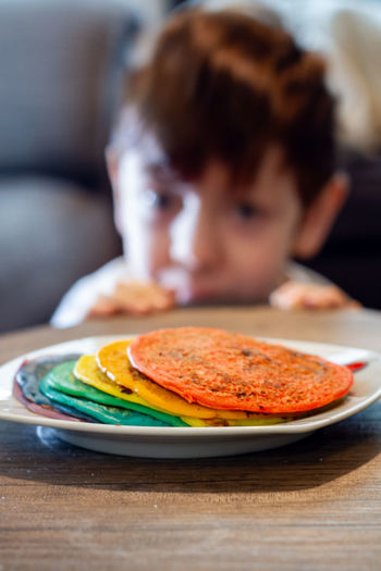 A plate of rainbow colored pancakes on a table with a cute boy looking in the background
