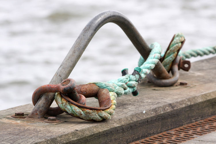 Close-up of rope tied to rusty metallic bollard on pier
