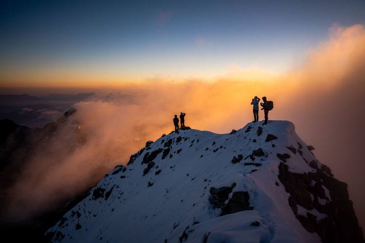 Silhouette people on snowcapped mountain against sky during sunrise