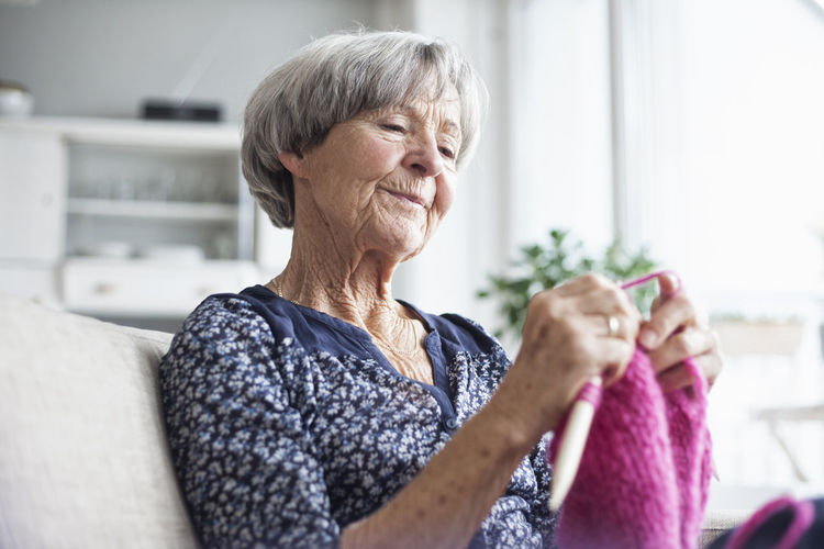 Portrait of knitting senior woman sitting on couch at home