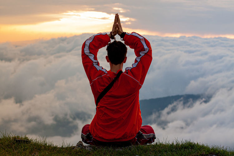 Rear view of man doing yoga on mountain peak against cloudy sky