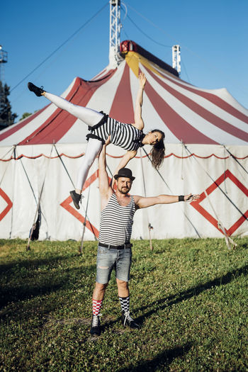Muscular male acrobat lifting female performer while standing on meadow