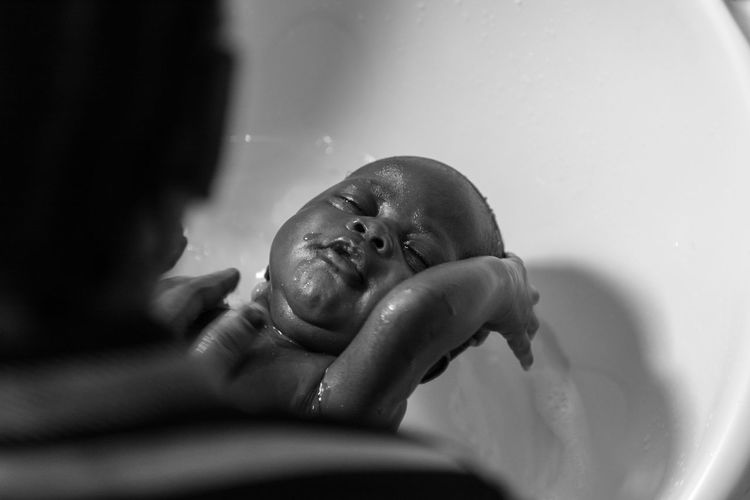 Cropped hands of parent bathing toddler son in bathtub