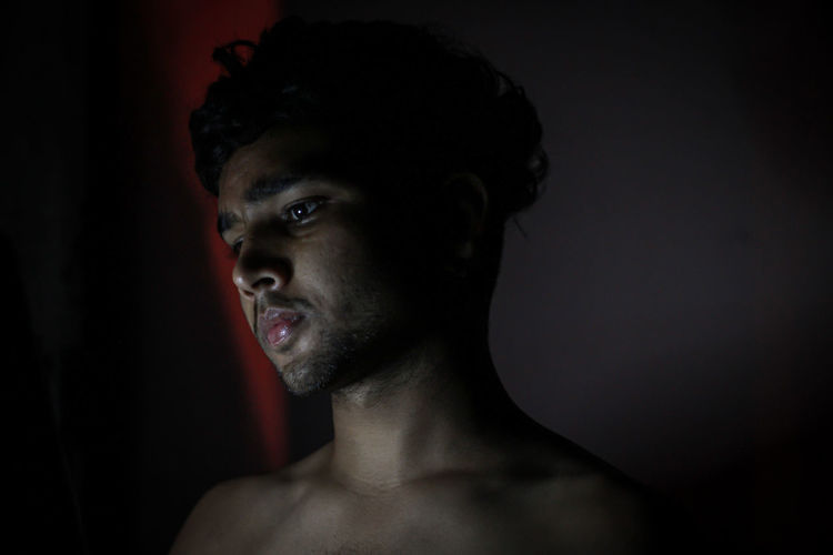 Portrait of young man looking away against black background