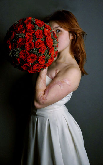 Portrait of woman holding roses bouquet against wall