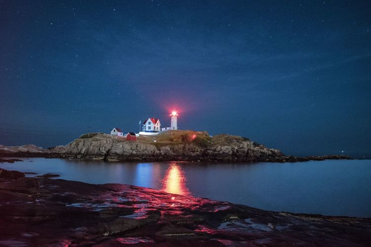 Reflection of illuminated lighthouse in water at night