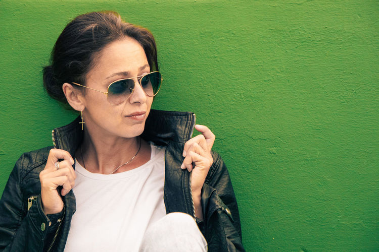 Portrait of young woman wearing sunglasses against wall
