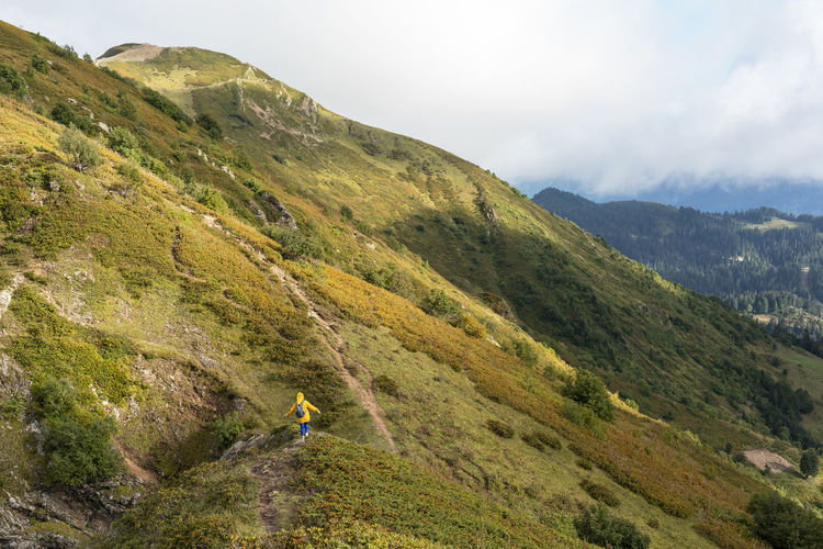 Rear view of young woman in yellow hoodie with backpack hiking in picturesque mountain valley view
