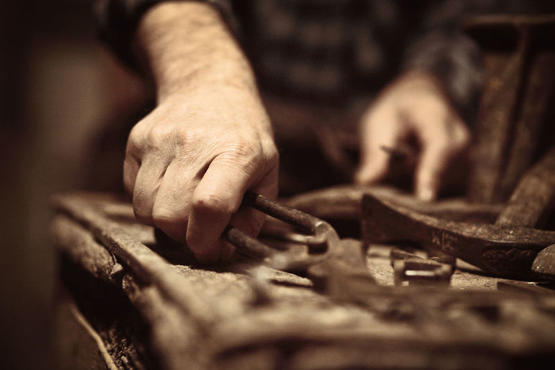 Cropped hand of manual worker holding work tool on table in workshop