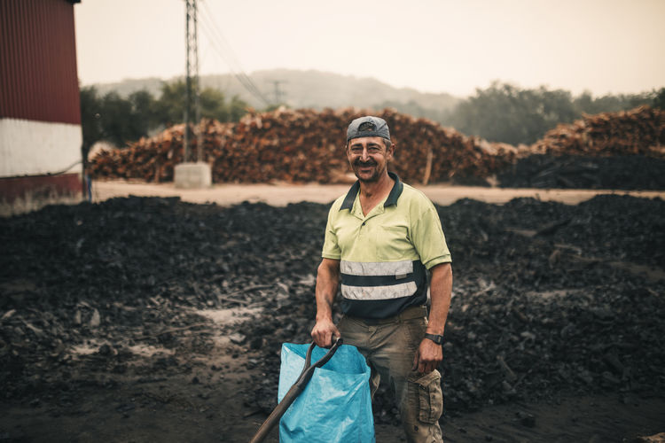 Smiling worker with plastic bag and tool standing at coal factory