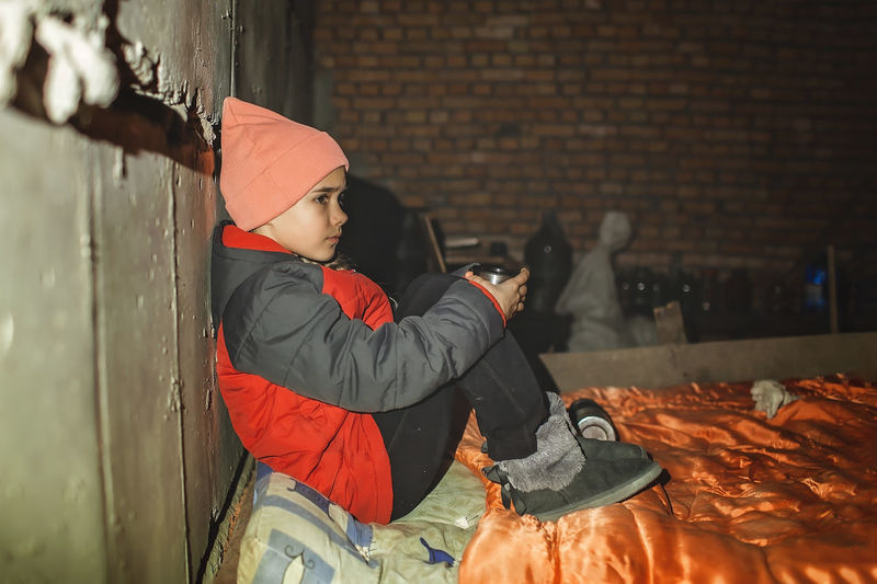 Side view of girl sitting on bed in shelter