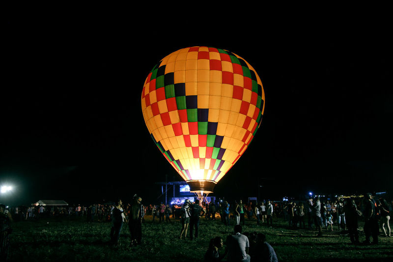 Illuminated hot air balloon and people on field at night 