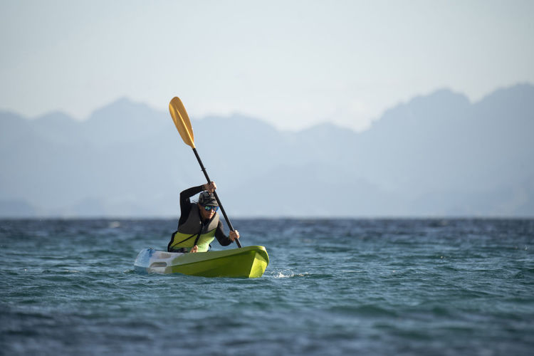 Man rowing boat in sea against mountains