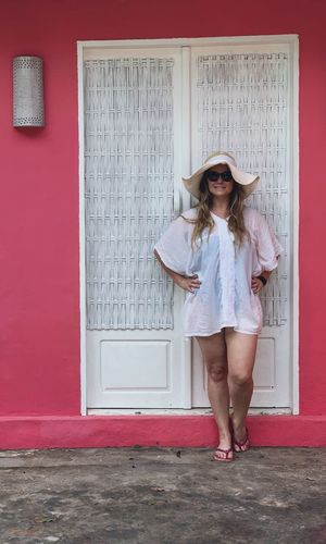 Portrait of woman wearing sunglasses and hat standing against wall