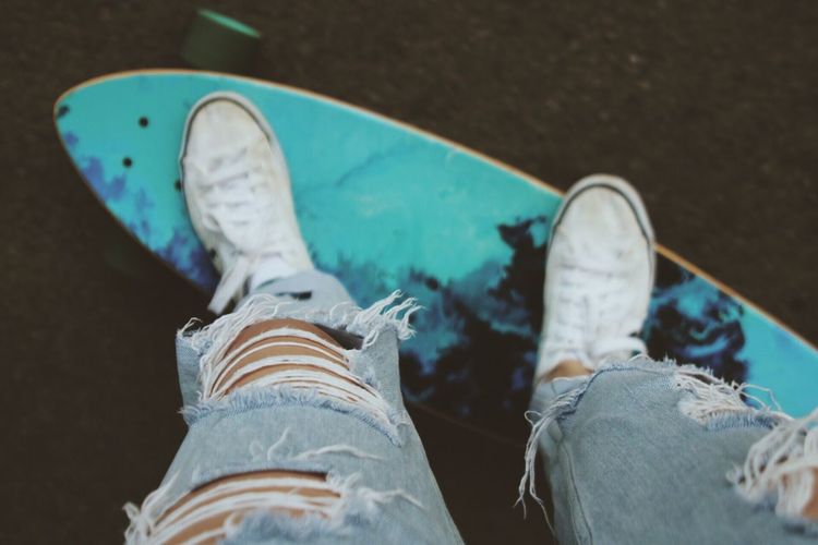 Low section of man with torn jeans standing on skateboard
