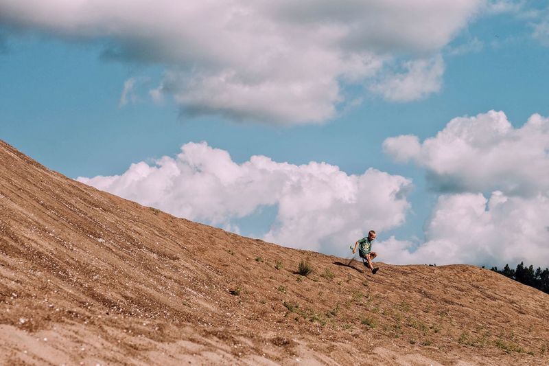 Low angle view of boy running down from hill against sky