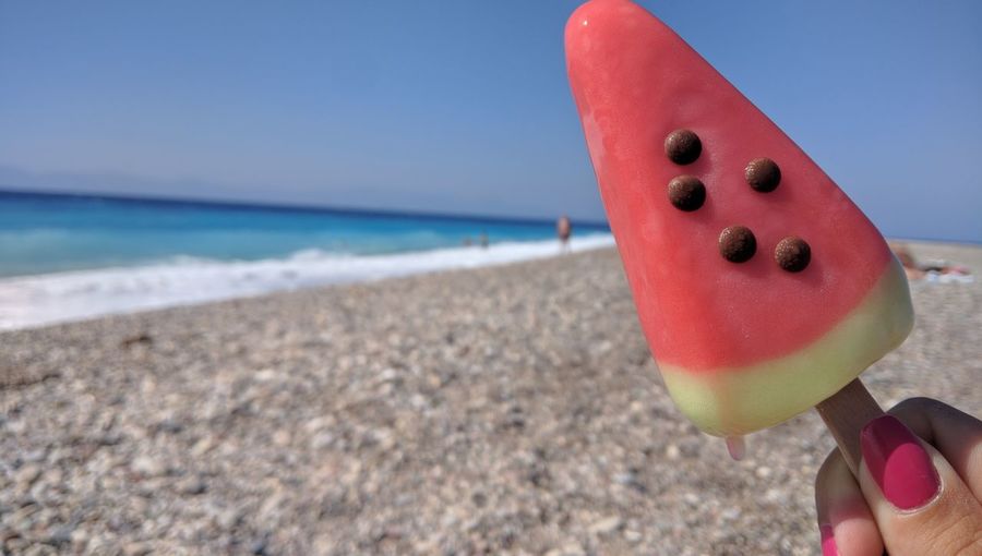 Cropped fingers holding watermelon shape ice cream at beach