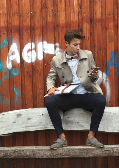 Young model using mobile phone while sitting on bench