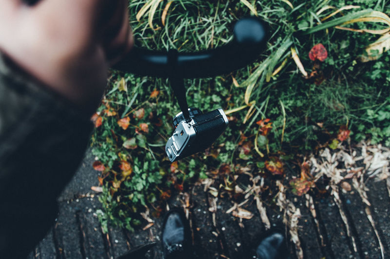 High angle view of man holding umbrella  hanging film camera against greenery and his own foots