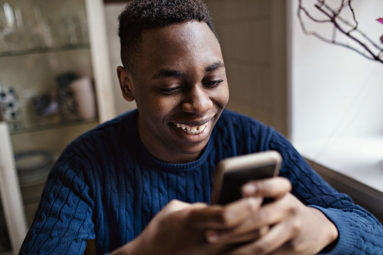 Smiling teenage boy using smart phone while sitting at home