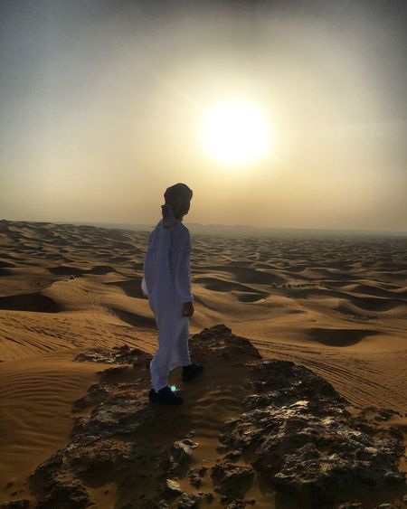 Man standing at desert against sky during sunset