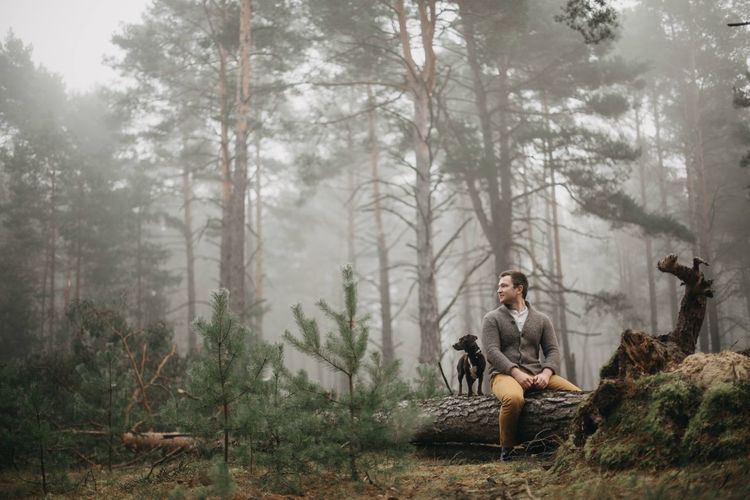 Man sitting with dog on fallen tree in forest