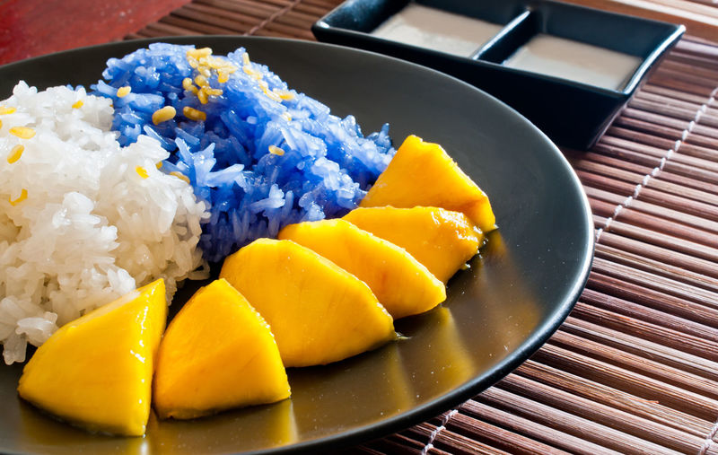 High angle view of white and blue rice with mango served in plate on place mat