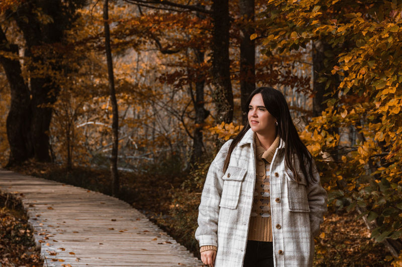 Portrait of young adult woman walking on wooden path in forest in autumn.