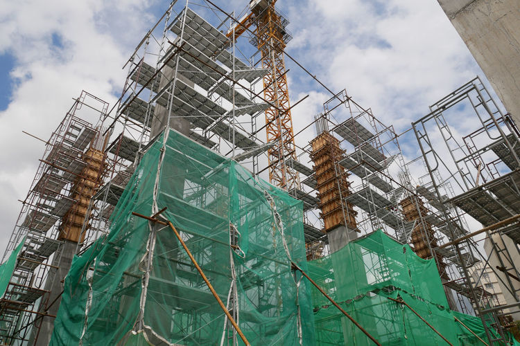 Low angle view of crane by building against sky