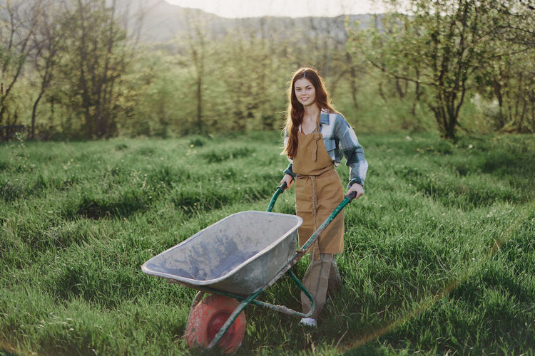 Portrait of young female farmer walking with wheelbarrow on field