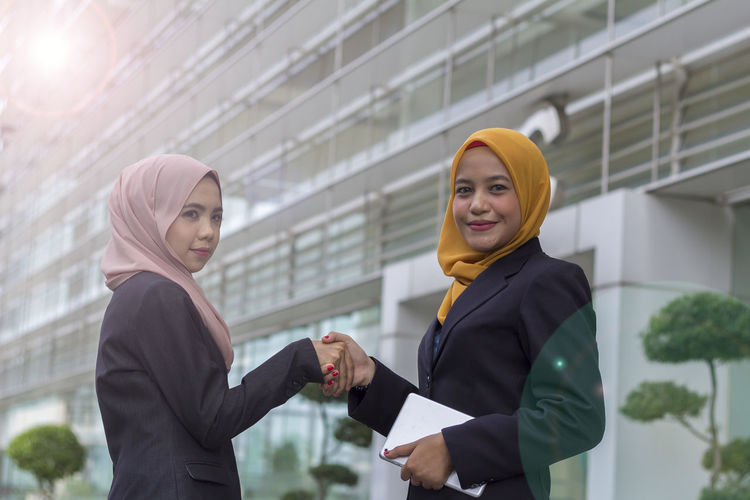 Businesswomen shaking hands while standing against office building