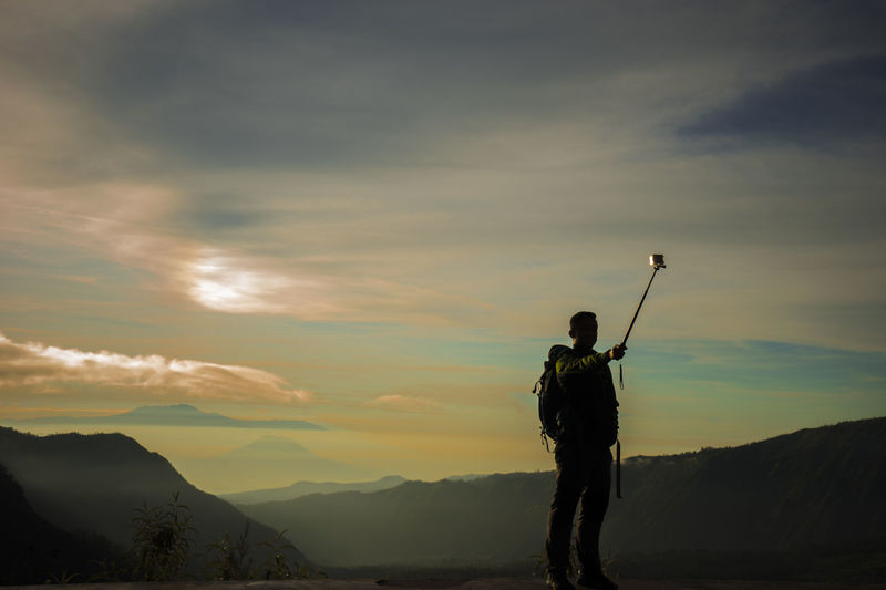 Silhouette of man photographing mountain at sunset