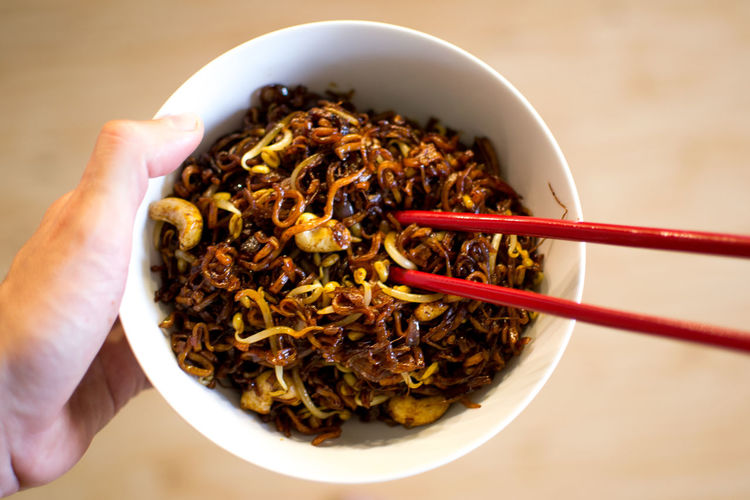 Cropped close-up of hand holding bowl with asian food