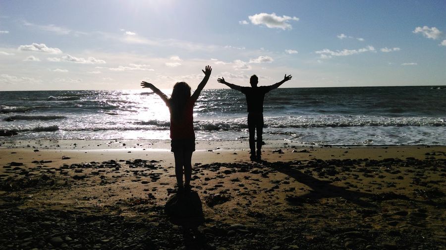 Rear view of father and daughter with arms outstretched standing at beach