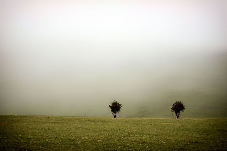 Two people walking on landscape against clear sky