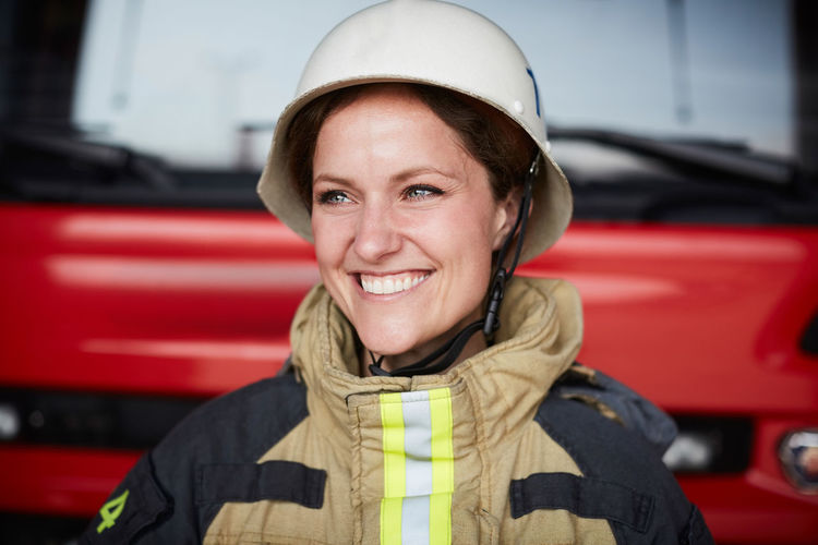 Smiling female firefighter wearing helmet looking away in fire station