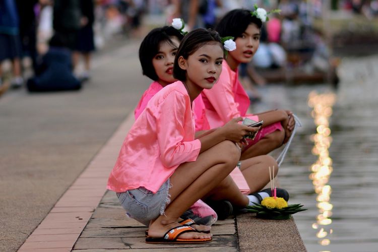 Young woman using mobile phone while sitting by lake in city